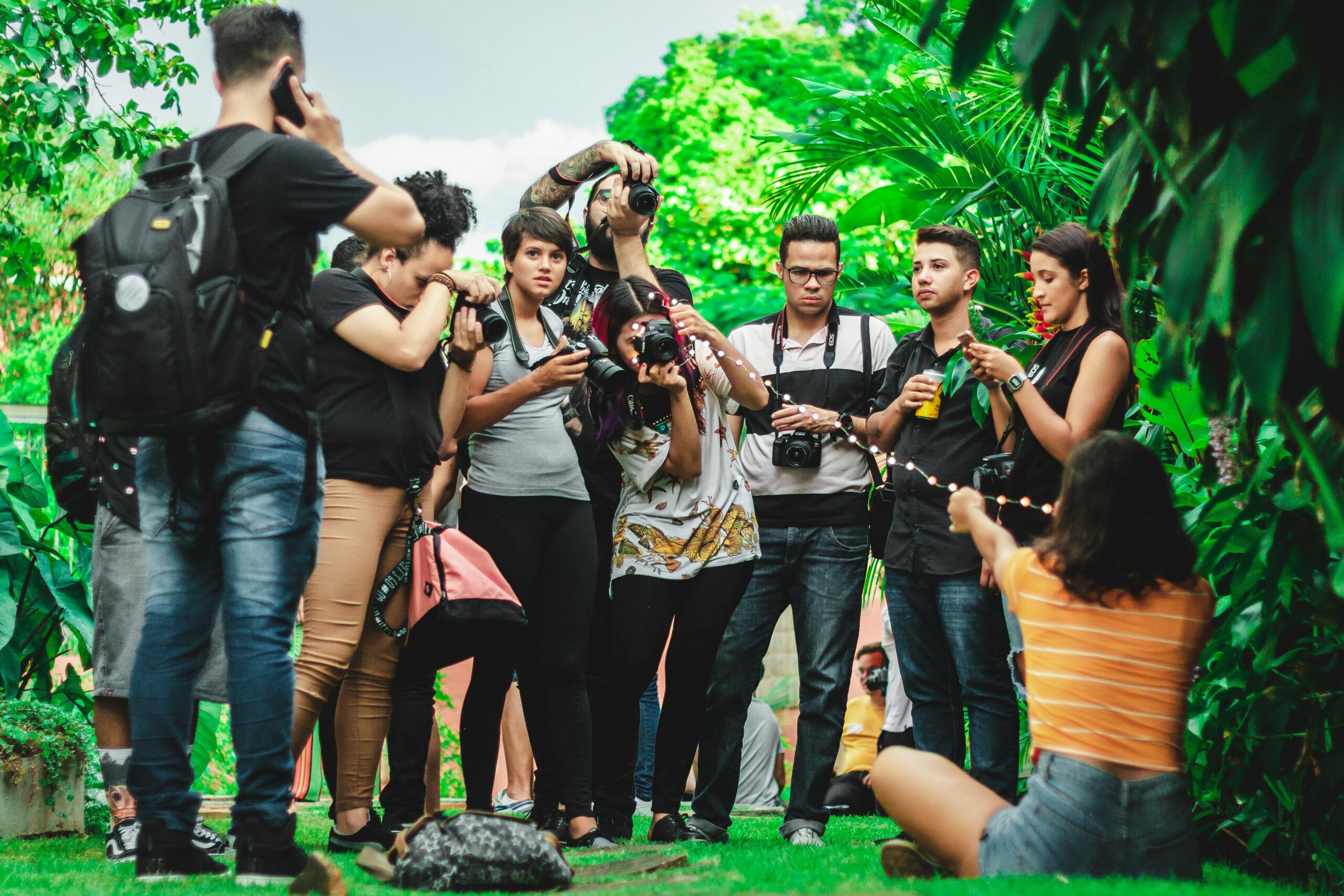A diverse group of photographers capturing moments outdoors amidst vibrant greenery.